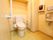 温水洗浄便座仕様のトイレで、横には手すりが設けられている。また、壁際には手拭きペーパーや手洗い場が設置されている。