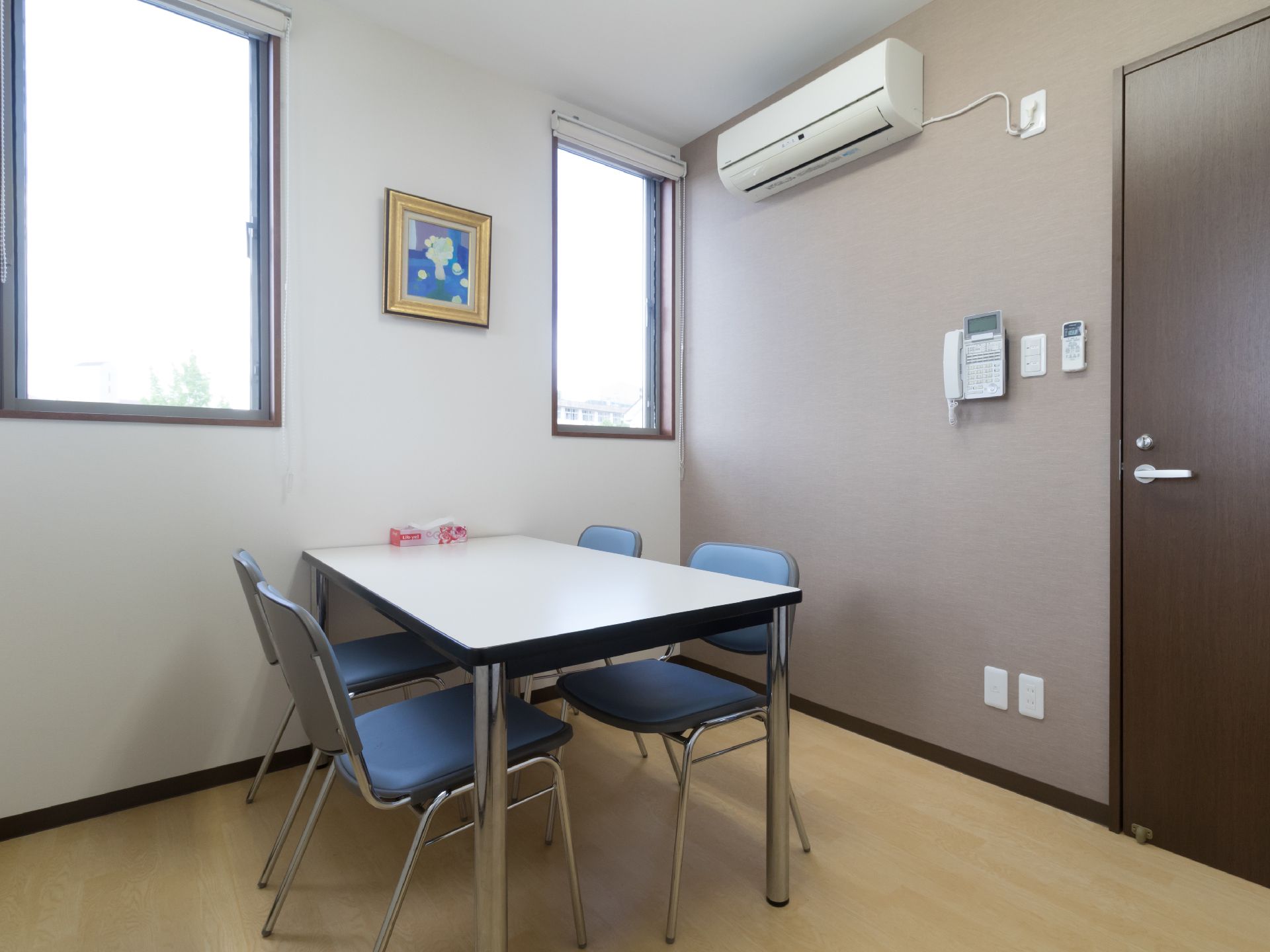 シンプルで明るい部屋には4人掛けのテーブルと椅子が置かれている。エアコンと電話機が壁に取り付けらている。