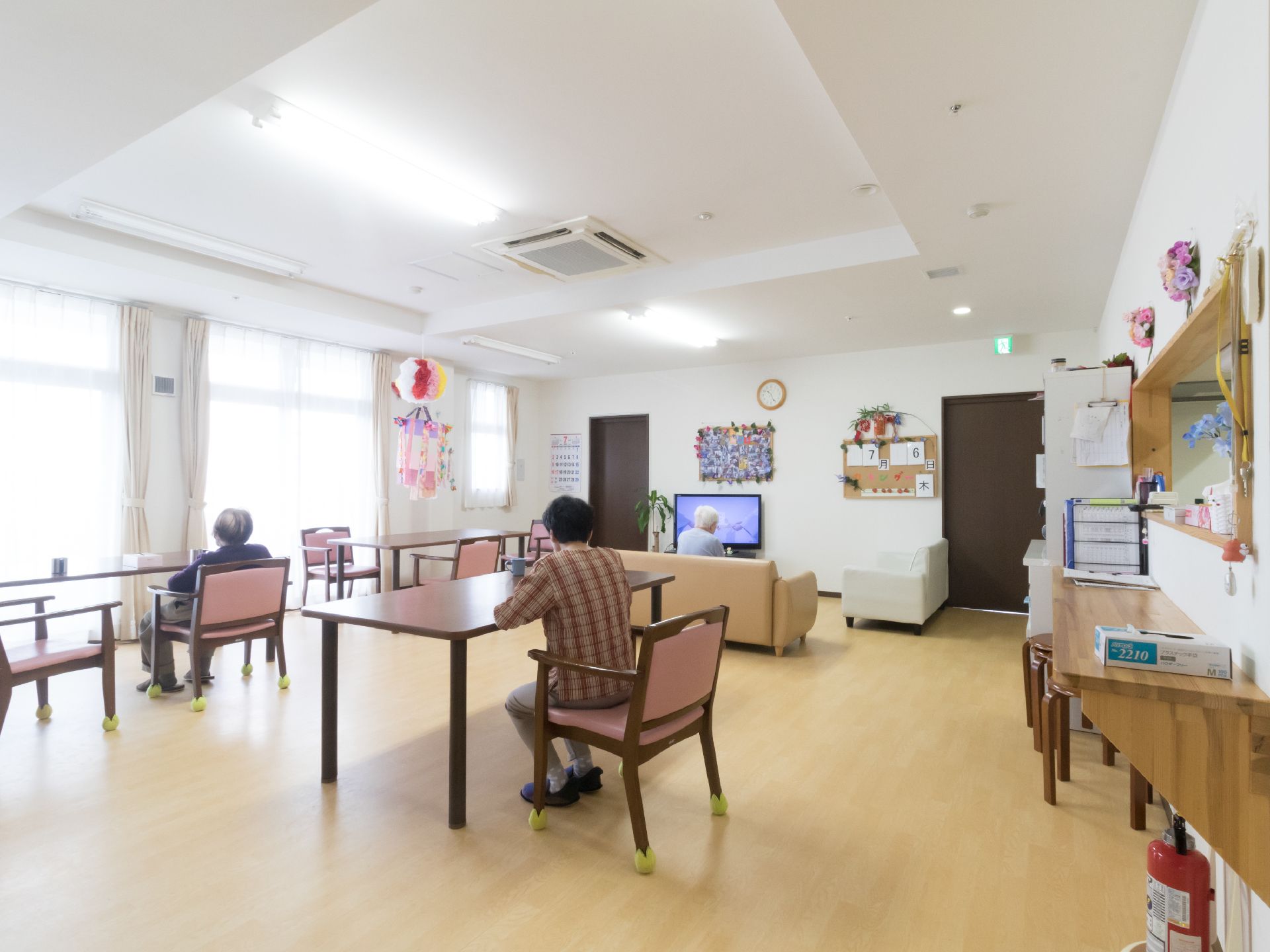 明るく広々としたリビングダイニングである。入居者の方々が食事をしたり、ゆったりとくつろいだりしている。