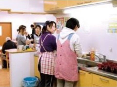 食堂の隣の台所で準備をするエプロンを着た女性スタッフ