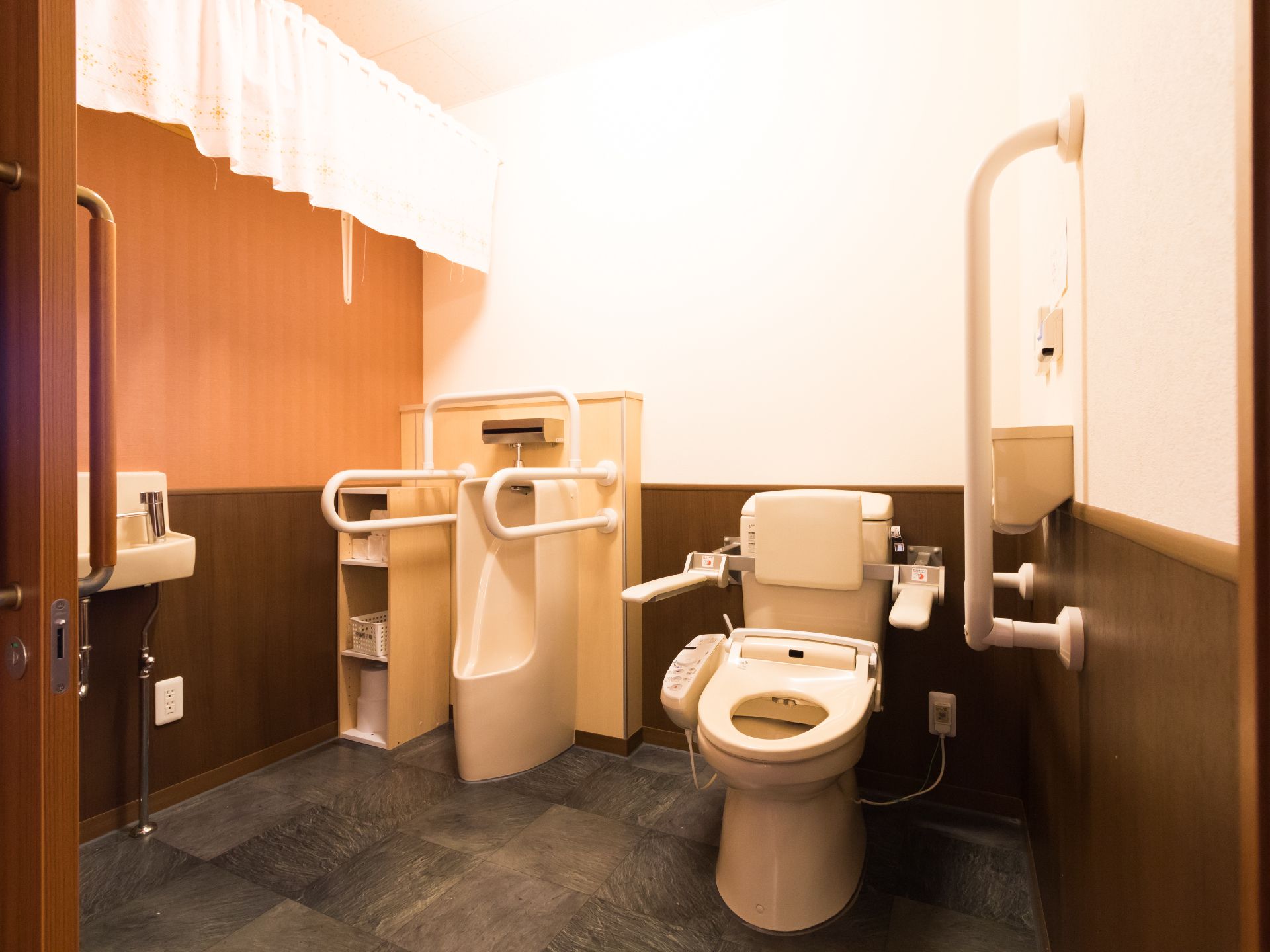 広い空間の共用トイレには洋式便器と男性用小便器が設置されている。洗面台も備え付けられている。手すりも取り付けてある。