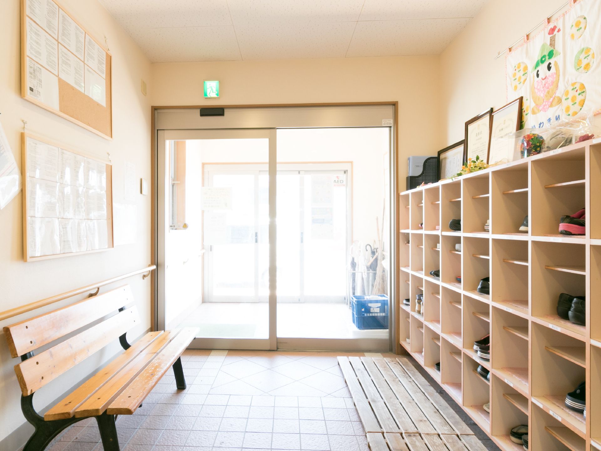 エントランスには、下足箱とベンチが設置されている。壁にはポスターなどが貼られている。ベンチは、靴を履いたり脱いだりするときに役立つ。
