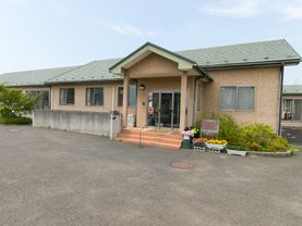 施設は、1階建てで、ベージュ系の壁に緑系の屋根である。建物の入り口前には、3段の階段があるが、真ん中に手すりがあり、摑まることができる。