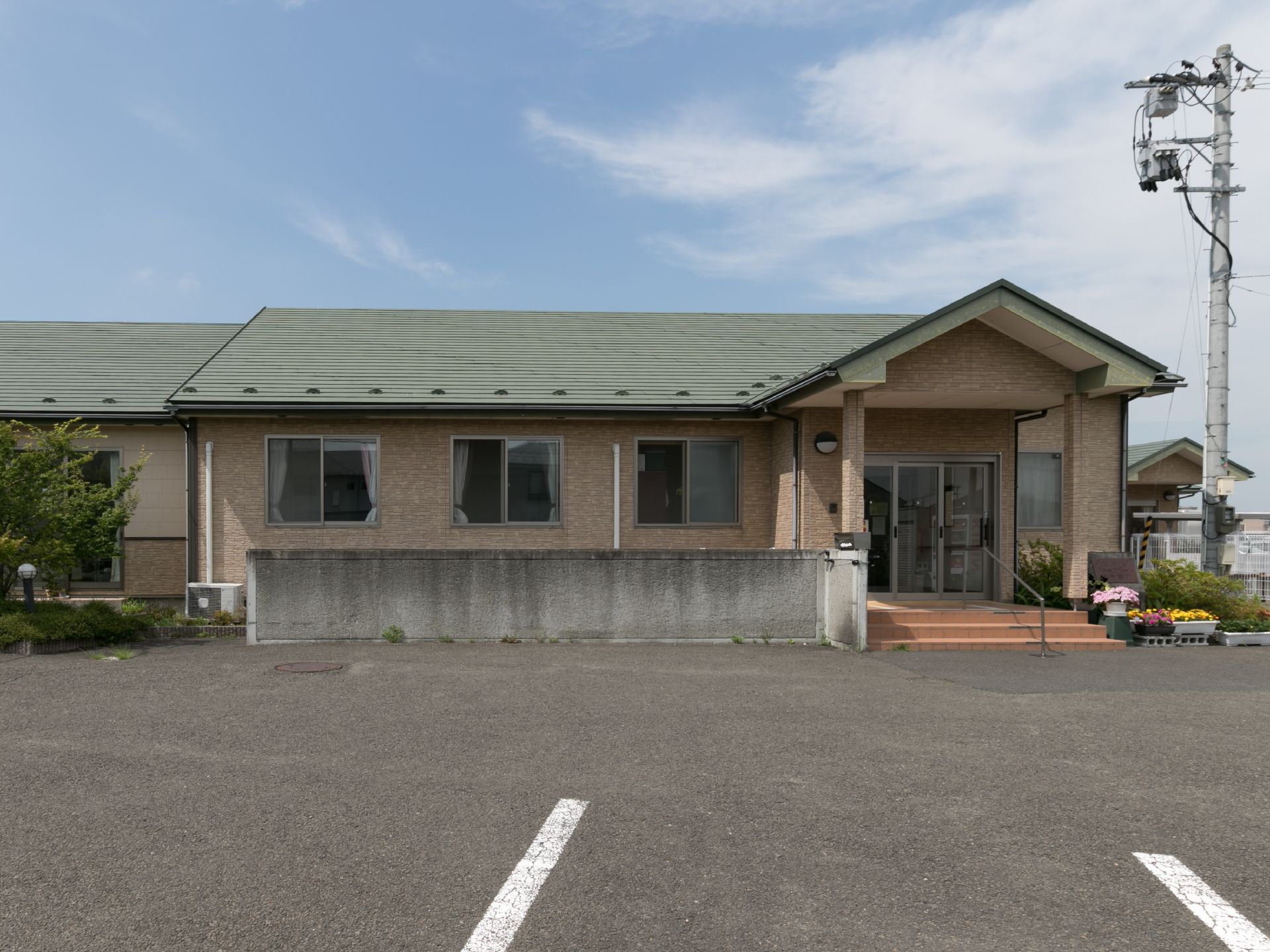 施設は平屋建て。壁はベージュ、屋根はグリーンで落ち着いた色合い。駐車場のスペースがかなりゆったりしており、駐車しやすい。