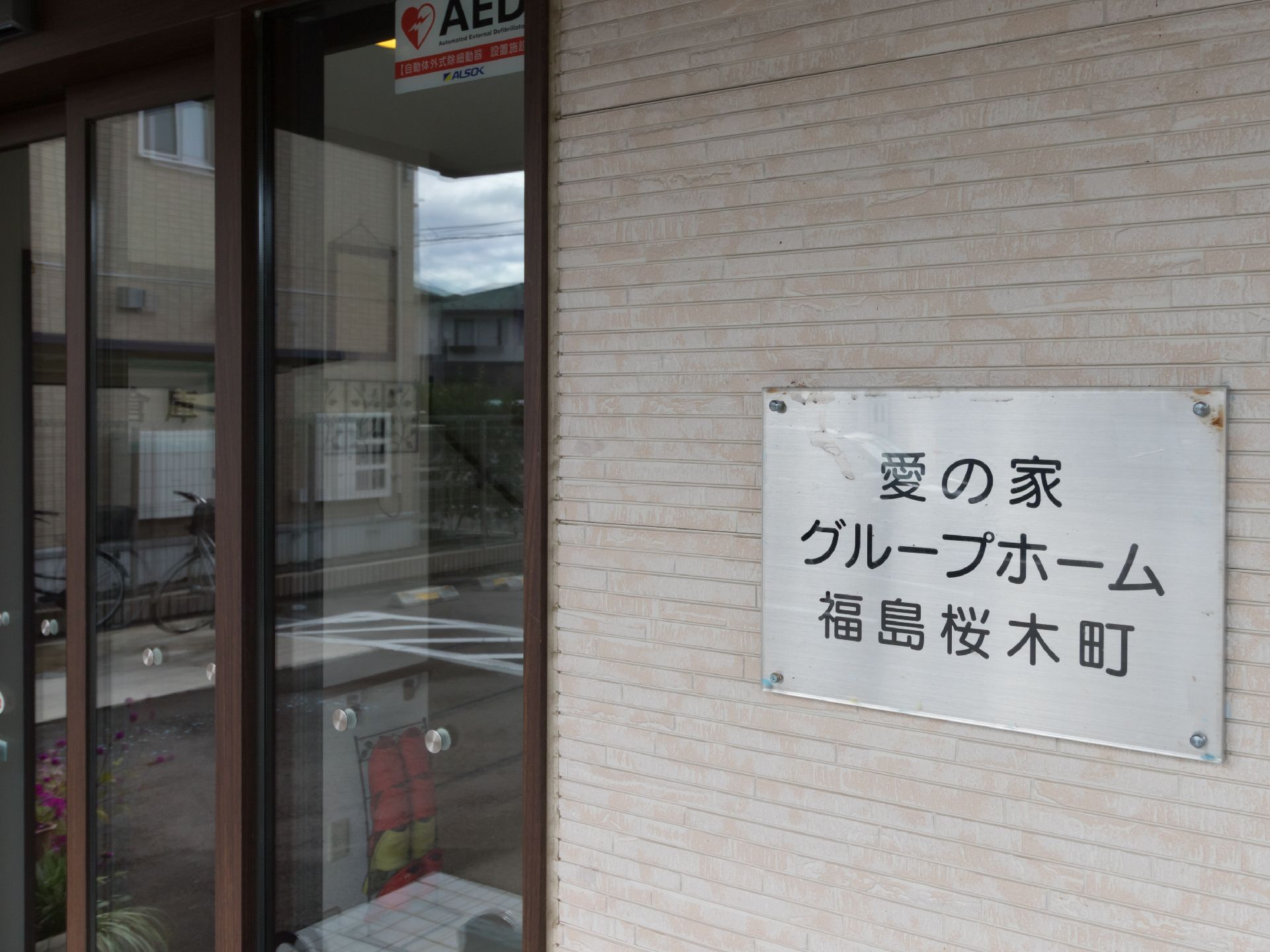 建物入口の透明ガラスの自動ドアとグループホームの看板