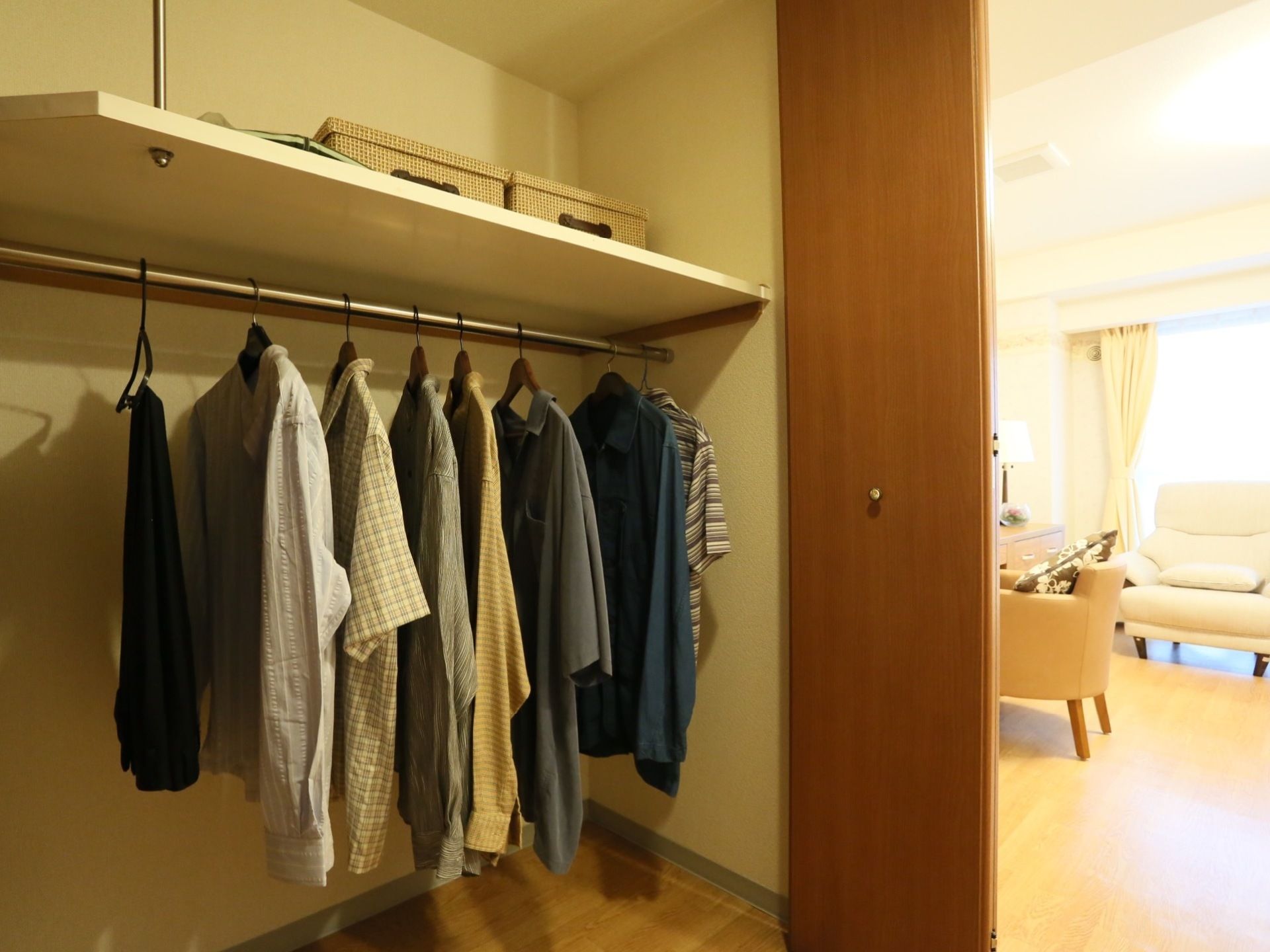居室にある扉の付いた大きなクローゼット。たくさんの衣服が吊るされている。上部分には棚があり、箱が置かれている。