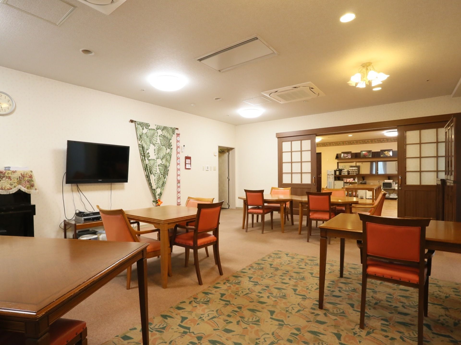 食堂の隣にある談話室。テーブルと椅子が並び、壁には大きなテレビが掛けられている。木製の大きなドアが食堂へと続いている。