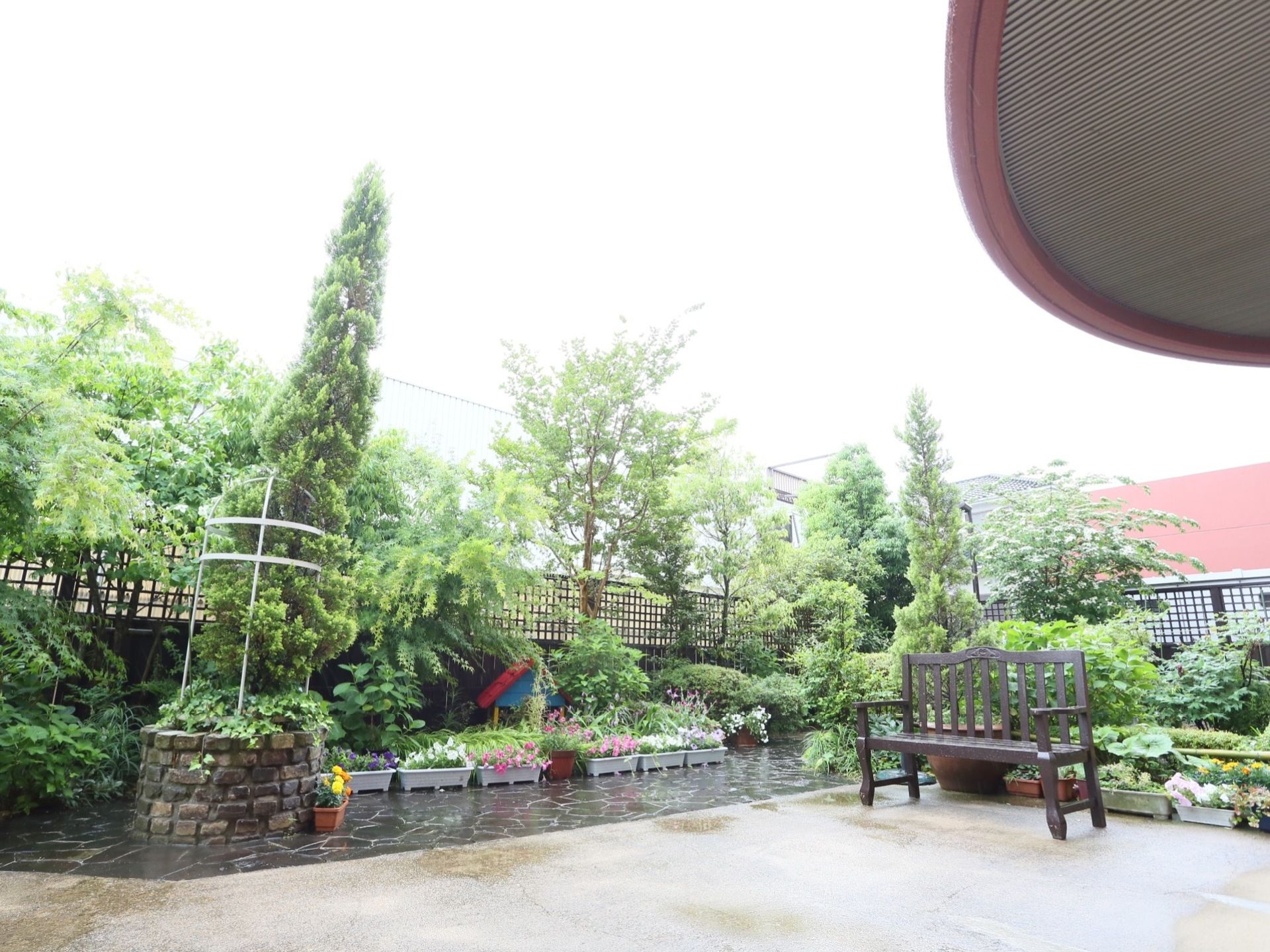 木のベンチが置かれた広い庭園がある。地面は舗装され、一部が石畳になっている。周囲は樹木で覆われ、黒い格子状のフェンスで囲まれている。
