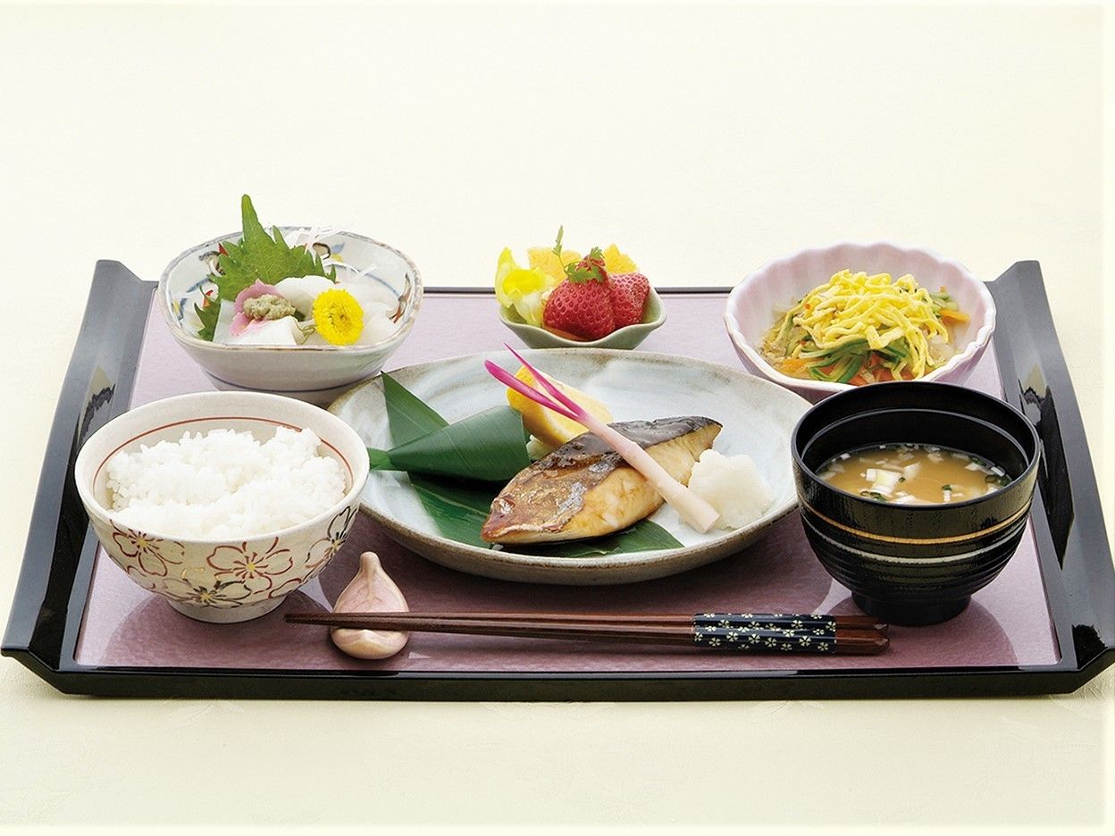 黒いお盆に焼き魚、ご飯、お味噌汁、お刺身などが載っている