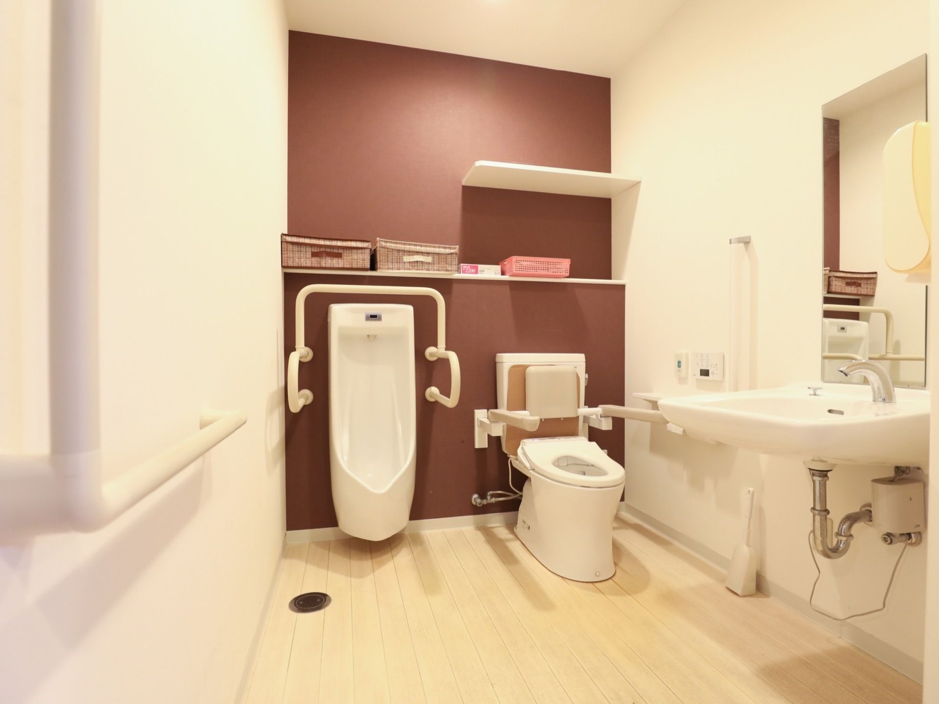 広々とした清潔なスペースに男性小用便器と洋式トイレ、洗面台が設置されている。手すりが設置されていて安全に利用できる。
