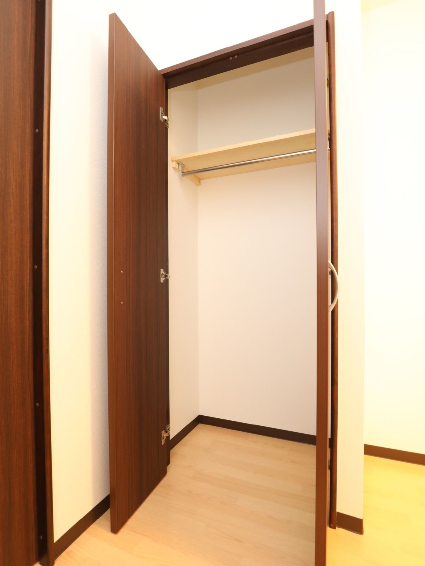 居室にはクローゼットが設置されている。落ち着いた色合いの扉を開くと、パイプハンガーと棚が一段取り付けられている。