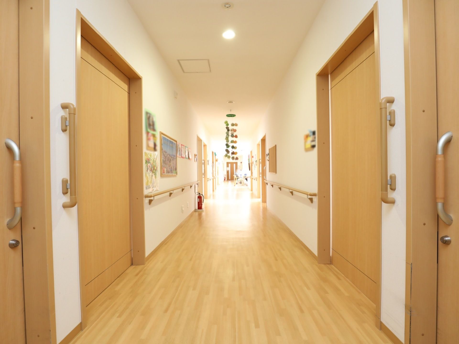白い壁に明るい木目調で統一された廊下である。災害対策として消火器が配備され、安全に移動できるように壁に手すりが設置されている。