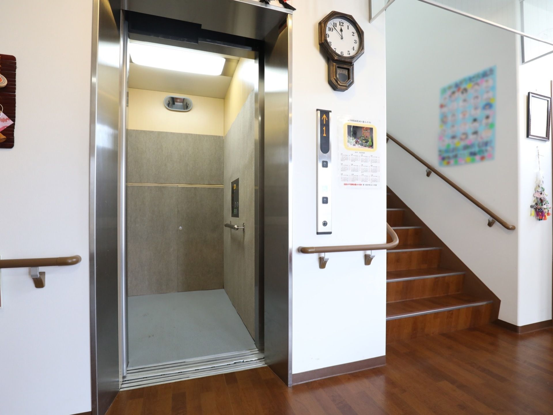 施設内に完備されているエレベーターである。扉は開かれ、横の壁にはクラシカルな柱時計が掛けられている。