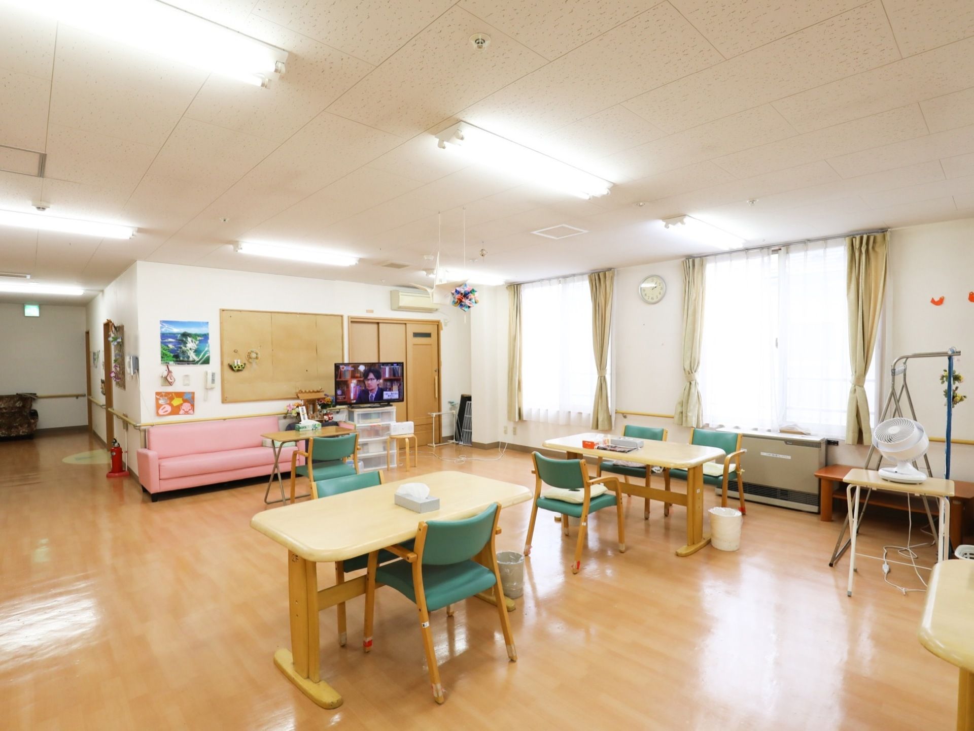 広々としたオープンスペースには、中央に４人用の食堂テーブルと椅子が配置され、壁際にテレビとピンクの長椅子が置いてある。