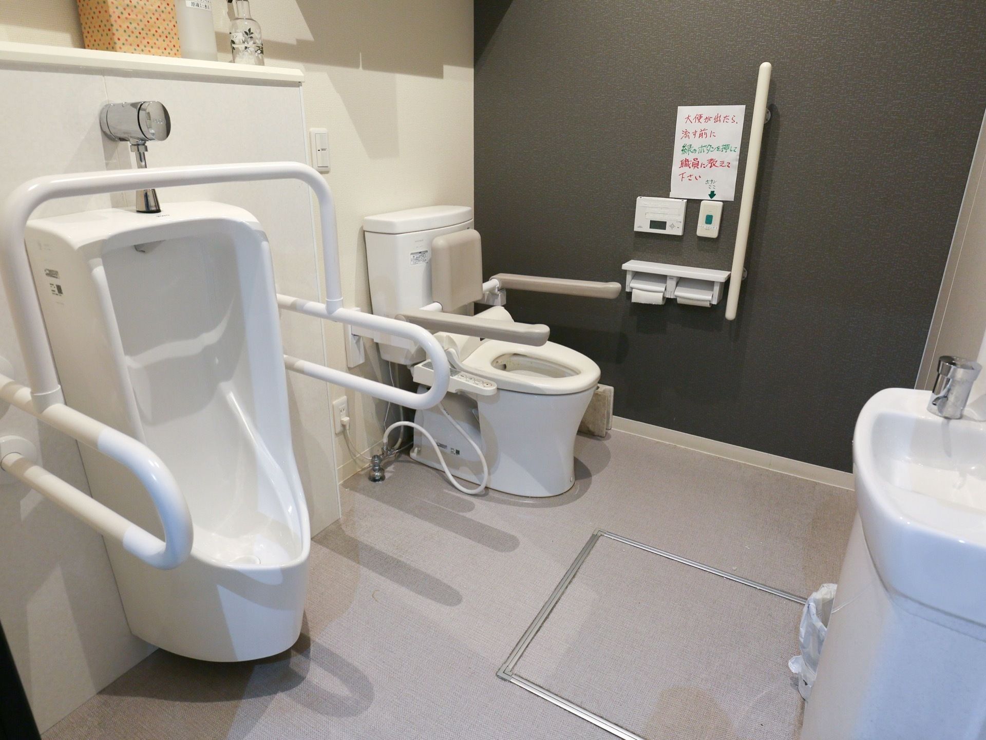 男性用の小便器、洋式便座が備え付けられたトイレである。随所に手すりが設置されている。手洗い場も完備。