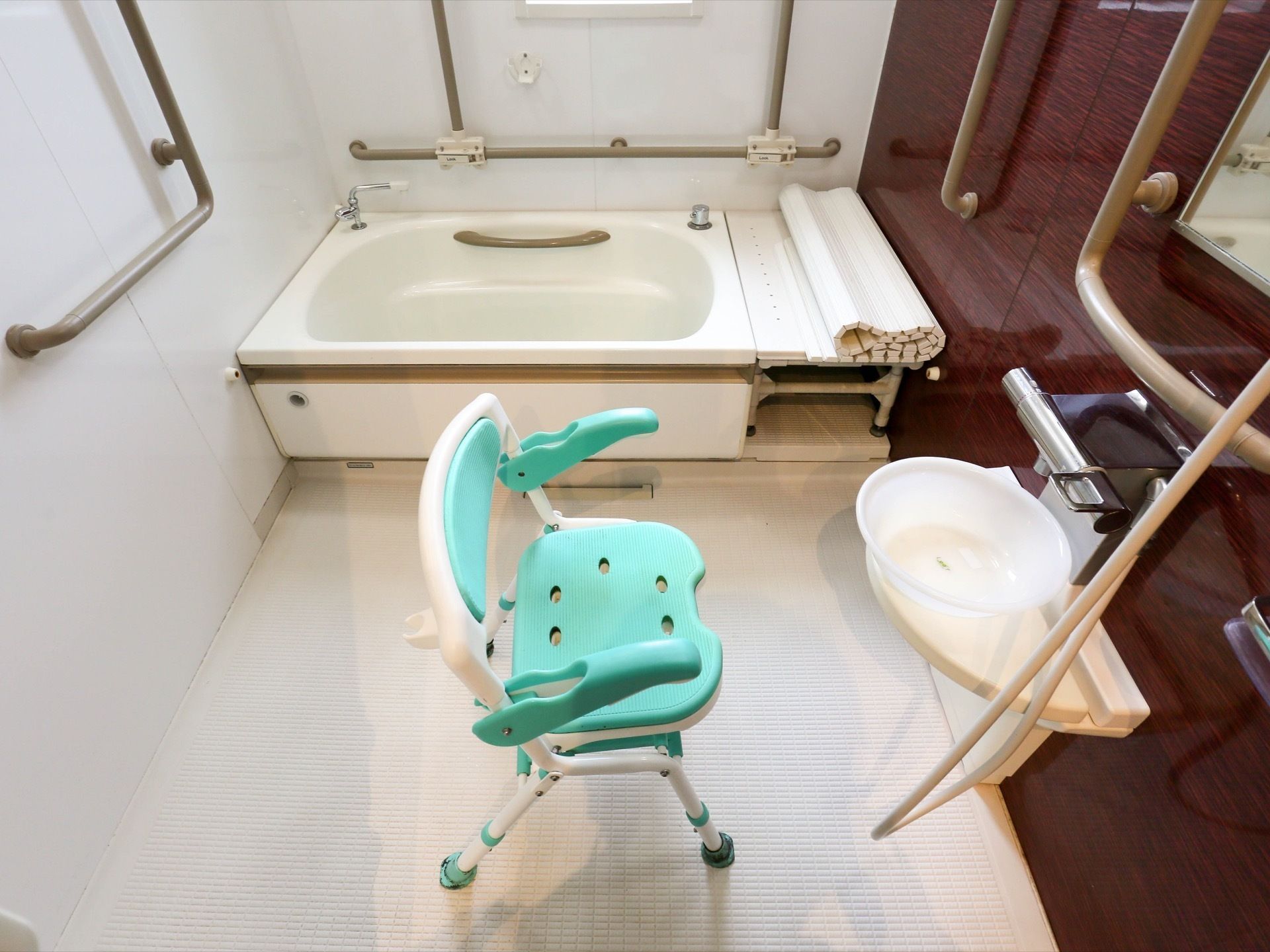 落ち着いたブラウンの壁色が、アクセントになった浴室である。複数の手すりが設けられている。シャワーチェアも完備。