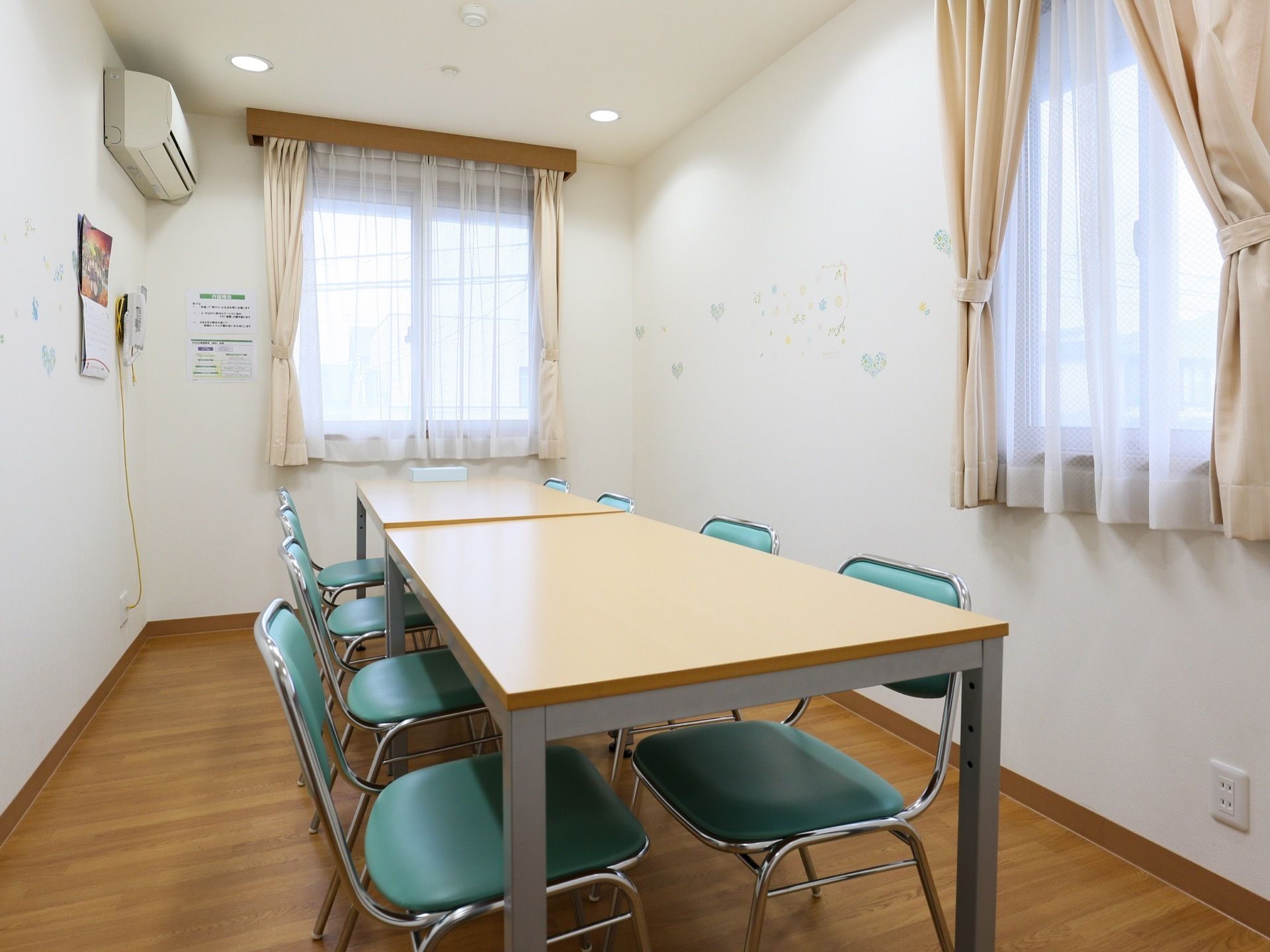 個室タイプの談話室の図である。部屋の中央にテーブルが２台あり、その周りに薄い水色の椅子が６脚並べられている。