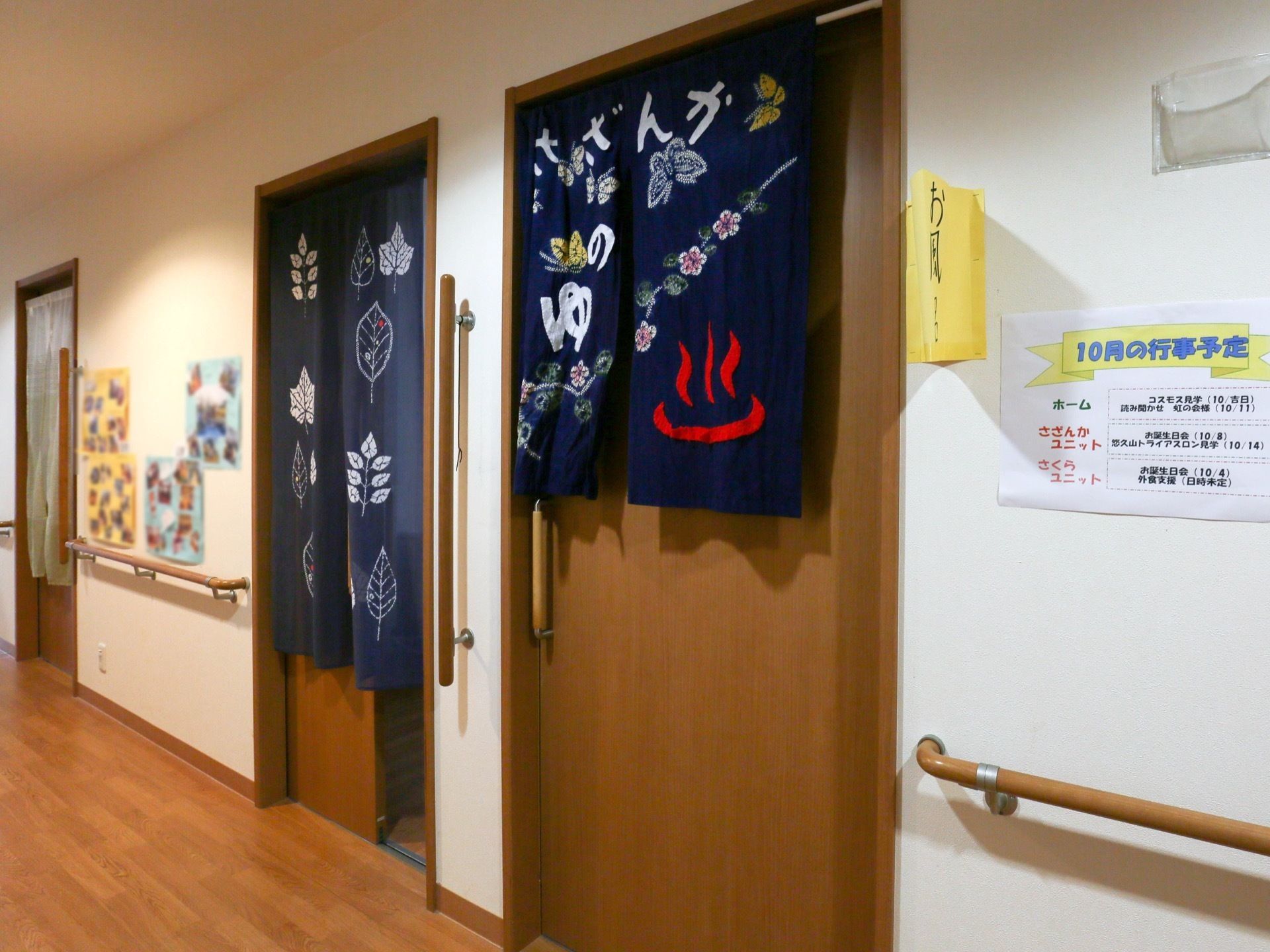 廊下に並ぶドアの図である。中央にあるドアは浴室へ続いており、紺色の布に赤い字で温泉のマークが描かれたのれんが下がっている。