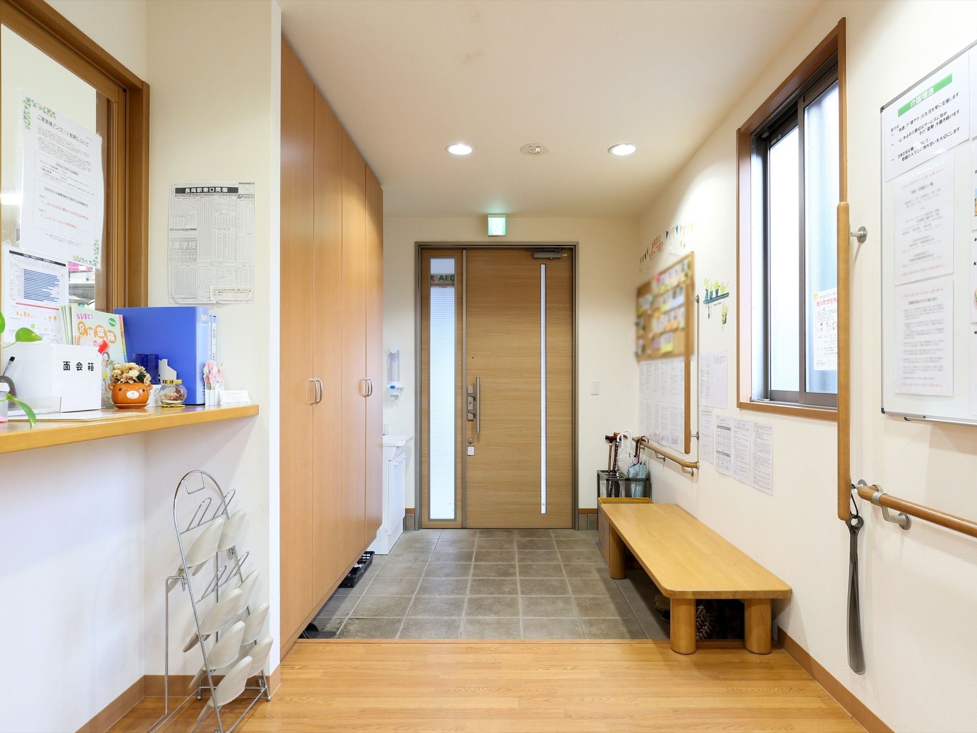 木材の床が広がるエントランスで、奧に入り口扉が見えている。ドアの上に非常口のライトが設置されている。