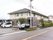 ２階建ての施設が中央に建っている。施設の前は道路が通っている。入り口前に白い車と黒い車が停められている。