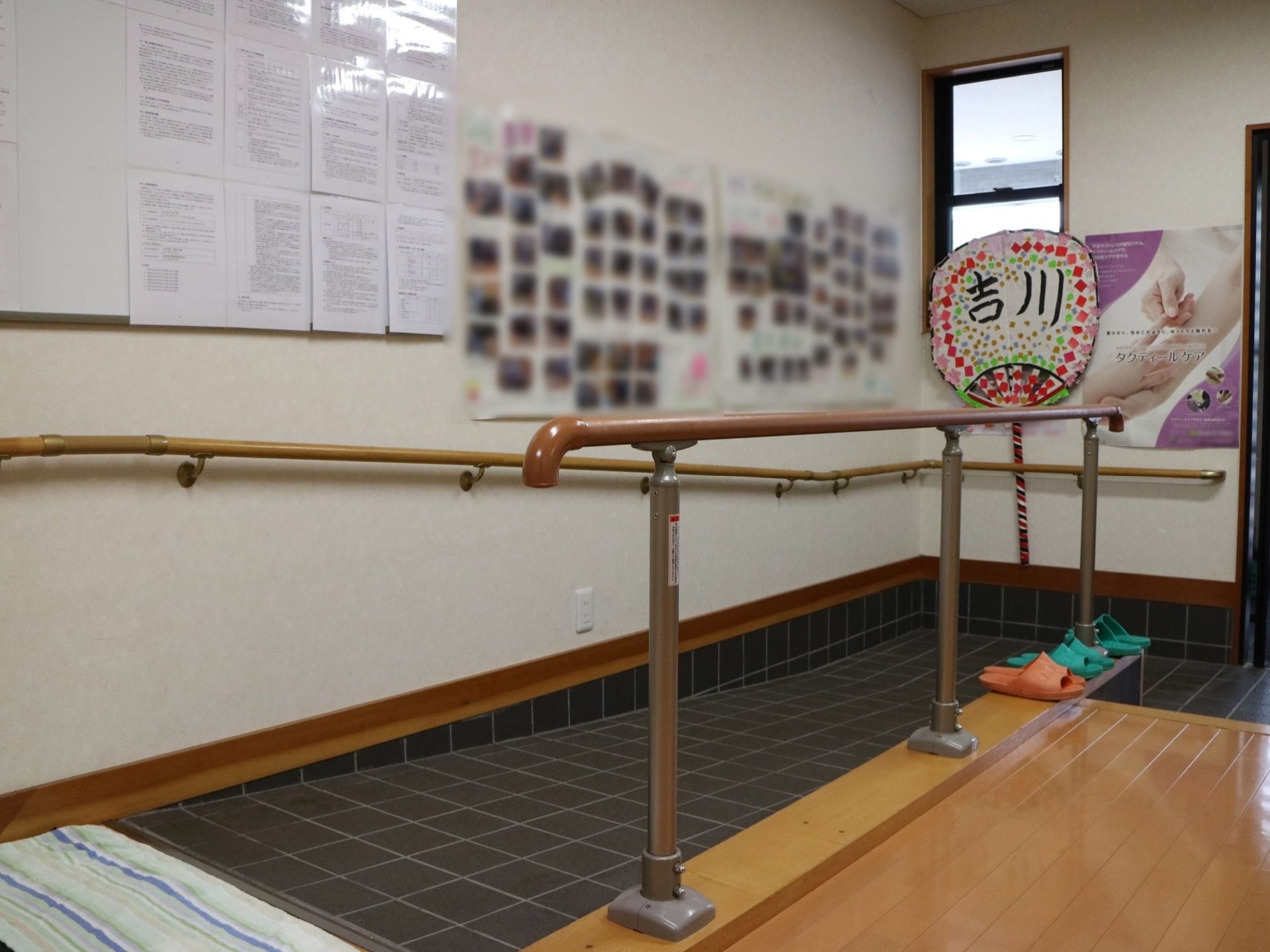 ダーク系の床色に施された玄関である。手すりが完備されたスロープもある。写真や手作り品が飾られている。