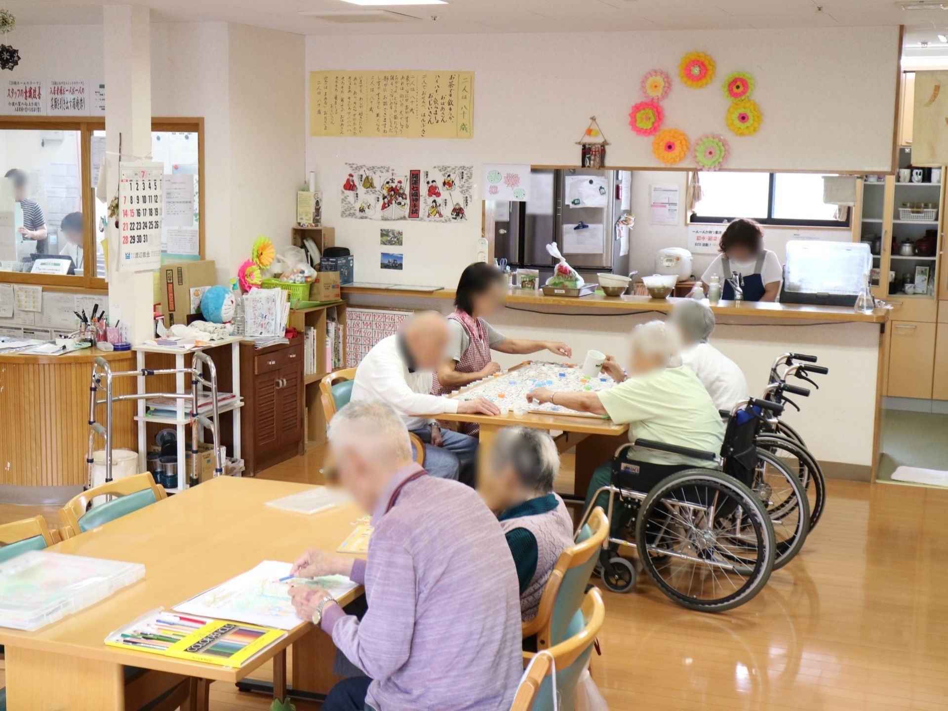 あたたかい色合いの共有スペースである。広々としたテーブルセットが置かれ、複数の入居者様が憩いの時間を過ごしている。