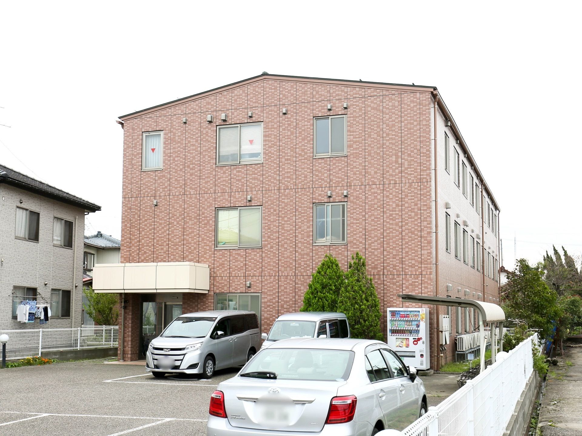 レンガ調の、落ち着いた色合いに施された外観である。施設は３階建て。エントランスには屋根が備えられている。