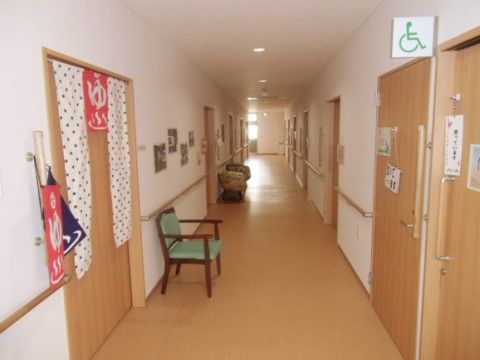 浴室やトイレのドアが並んだ廊下である。トイレの使用中サインや入浴前後の休憩用に置かれた椅子など、細かい気遣いが各所に盛り込まれている。