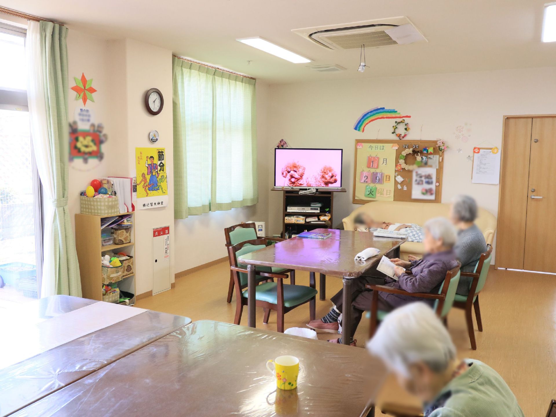 窓のある共有スペースには、テーブルセットやテレビが設置されている。3名の女性の入居者様がくつろがれている。