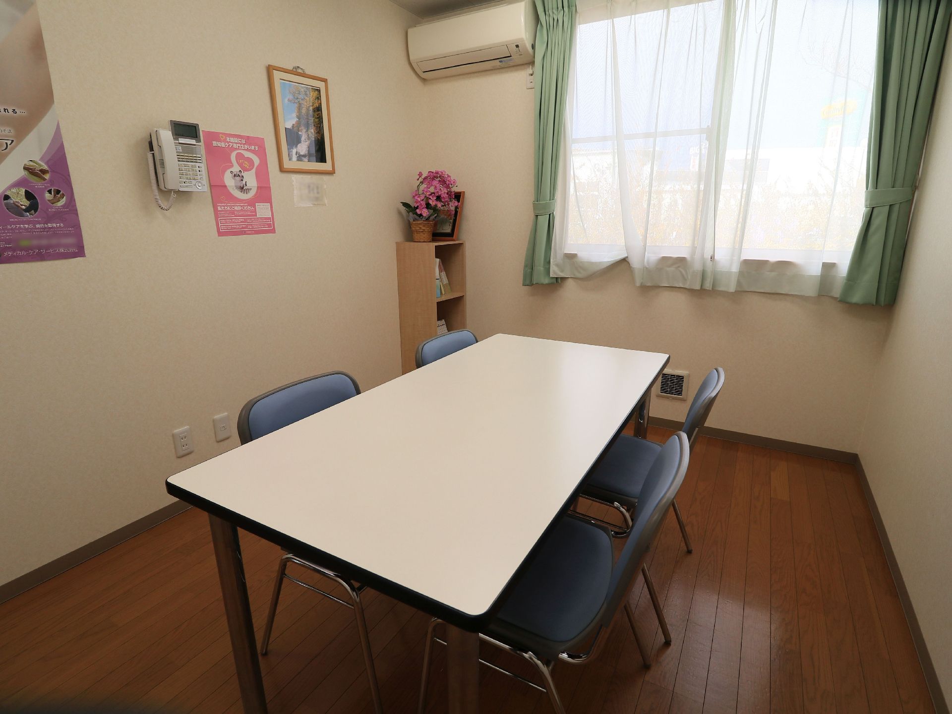 窓やエアコンが設置されている相談室には、4人掛け用の白いテーブルに青いシートの椅子が配置されている。