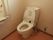 温水洗浄便座機能付きのトイレである。壁にはＬ字型の手すりとペーパーホルダー、操作パネルが設置されている。