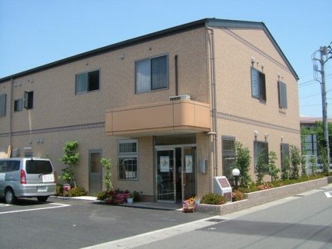 アットホームな雰囲気の２階建ての建物があり、そばに車が停まっている。建物沿いの植栽に植えられた木々が美しい。