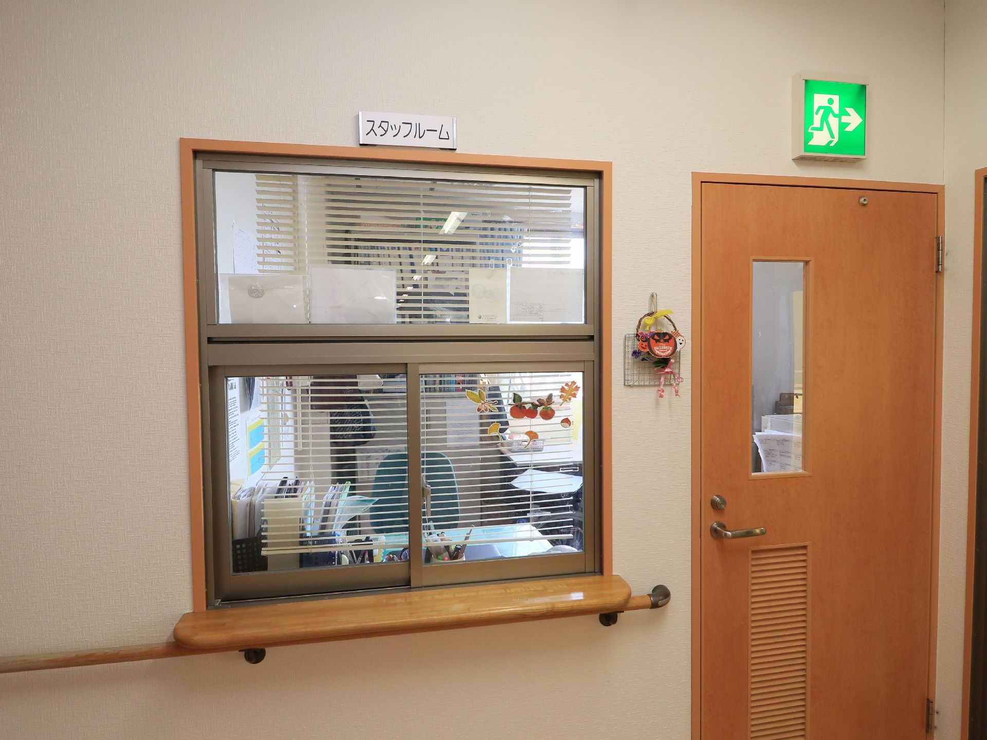 ガラス戸のはめられたカウンター窓口があり、上にスタッフルームと表示されている。横にはウッド調の扉がある。