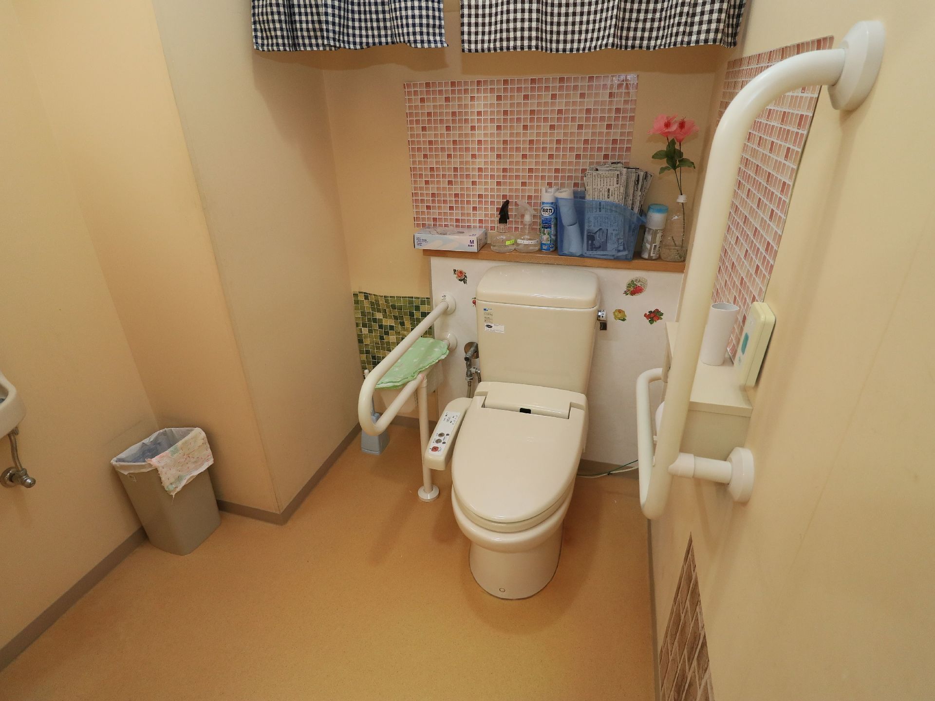 トイレは２か所に白い手すりが取りつけられている。後ろと横の壁にはモザイクタイル風のシートが貼られている。