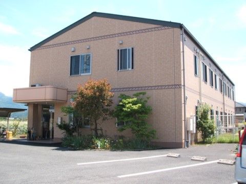 アットホームな雰囲気の２階建ての建物がある。周りに木々が植えられている。そばに駐車スペースが用意されている。