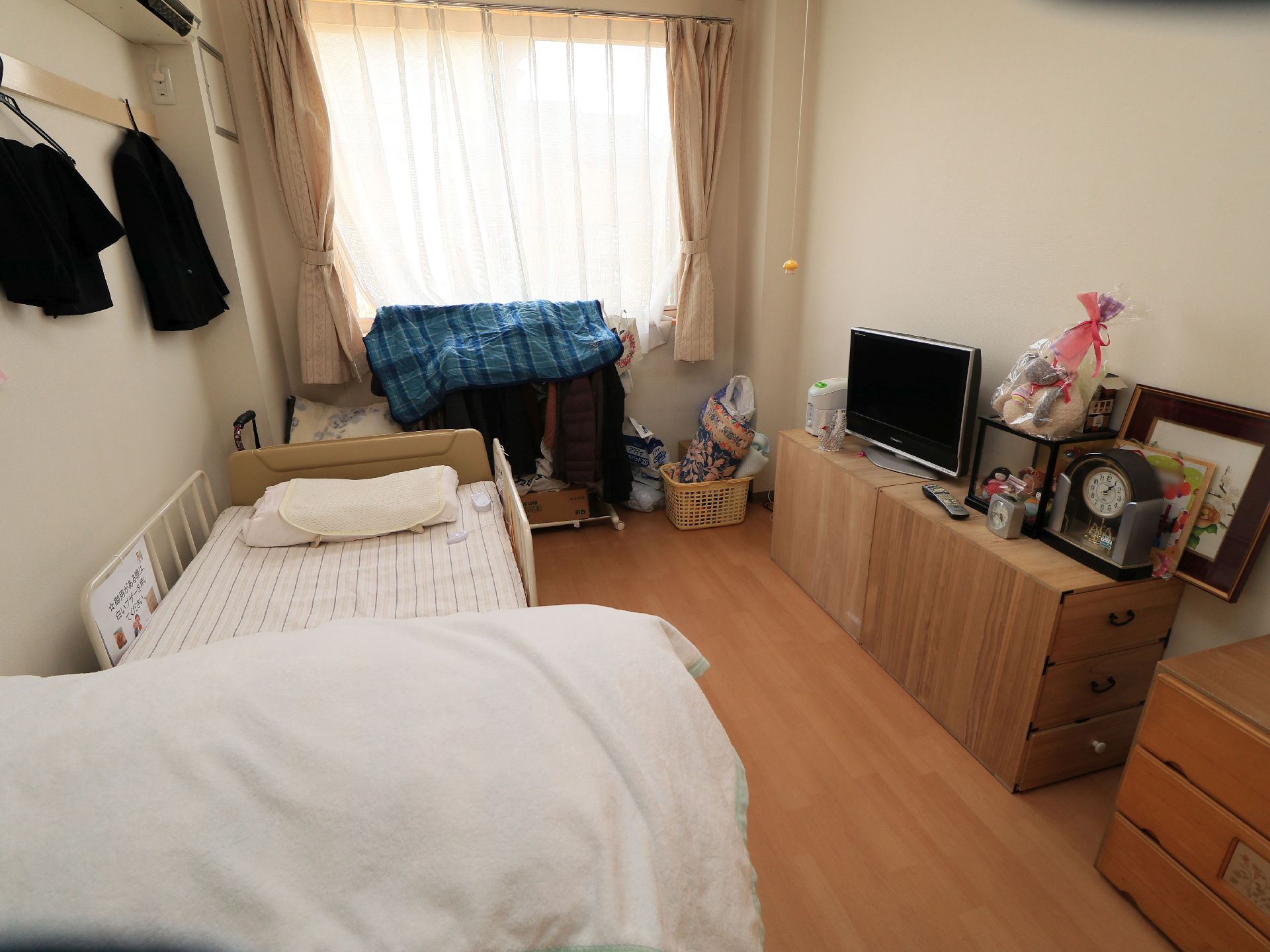 居室にはベッドやエアコン、テレビ、時計などが設置されている。収納家具はナチュラルな木目調で統一されており、明るい雰囲気である。