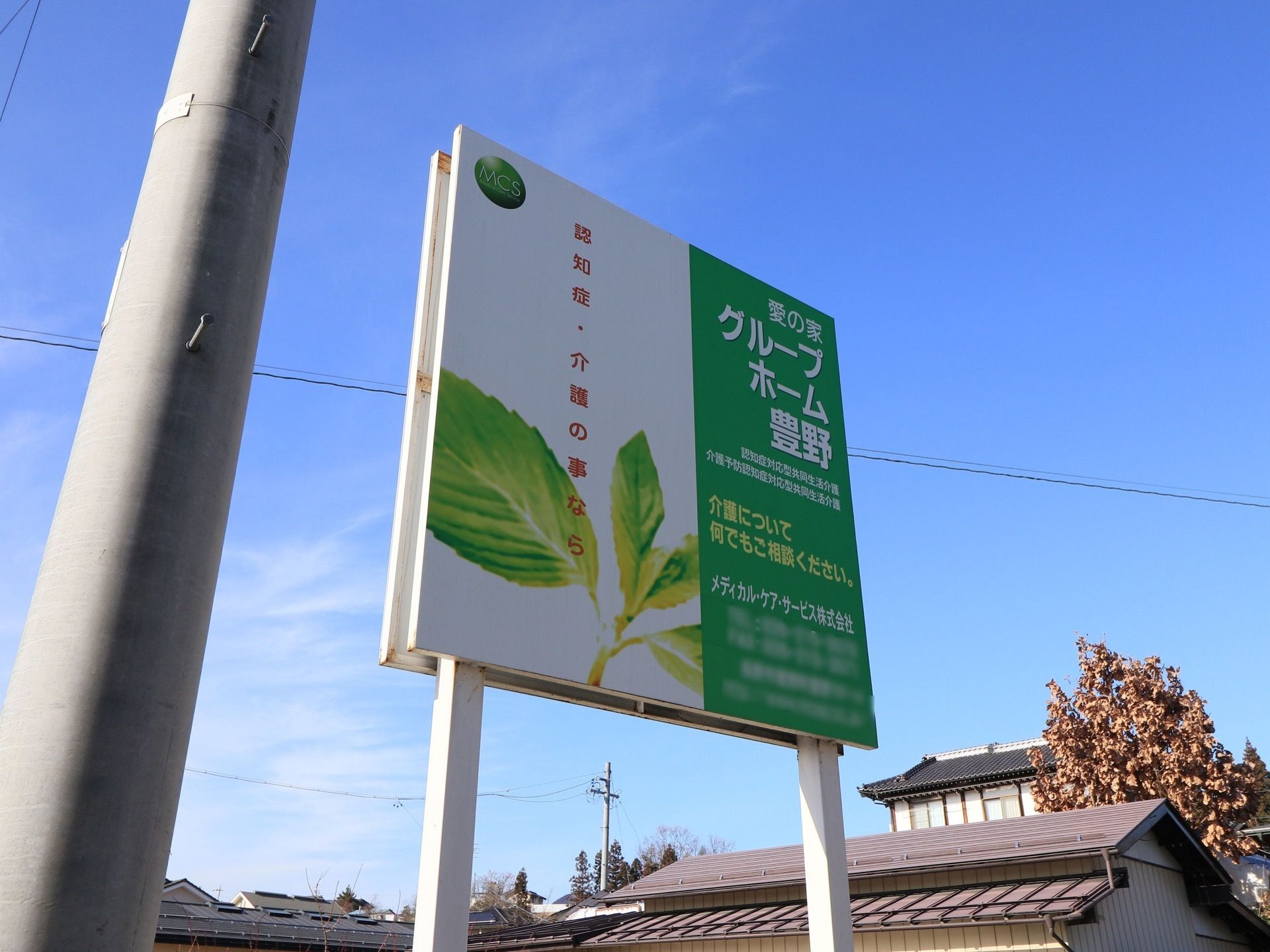 緑と白を基調とした施設の大きな看板がある。施設の特徴と連絡先が書かれ、若葉のイラストが描かれている。