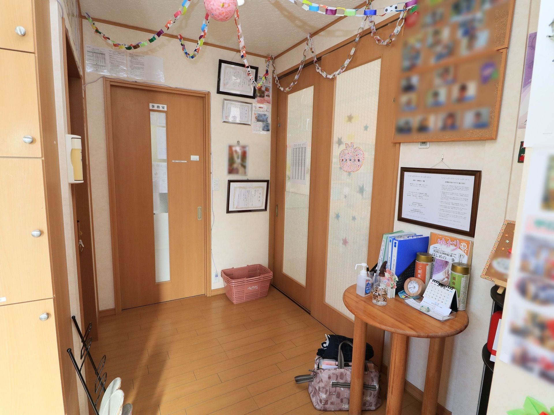玄関は、天井や壁に写真や手作りの飾りつけがされている。丸いミニテーブルがあり、冊子やカレンダーが置かれている。