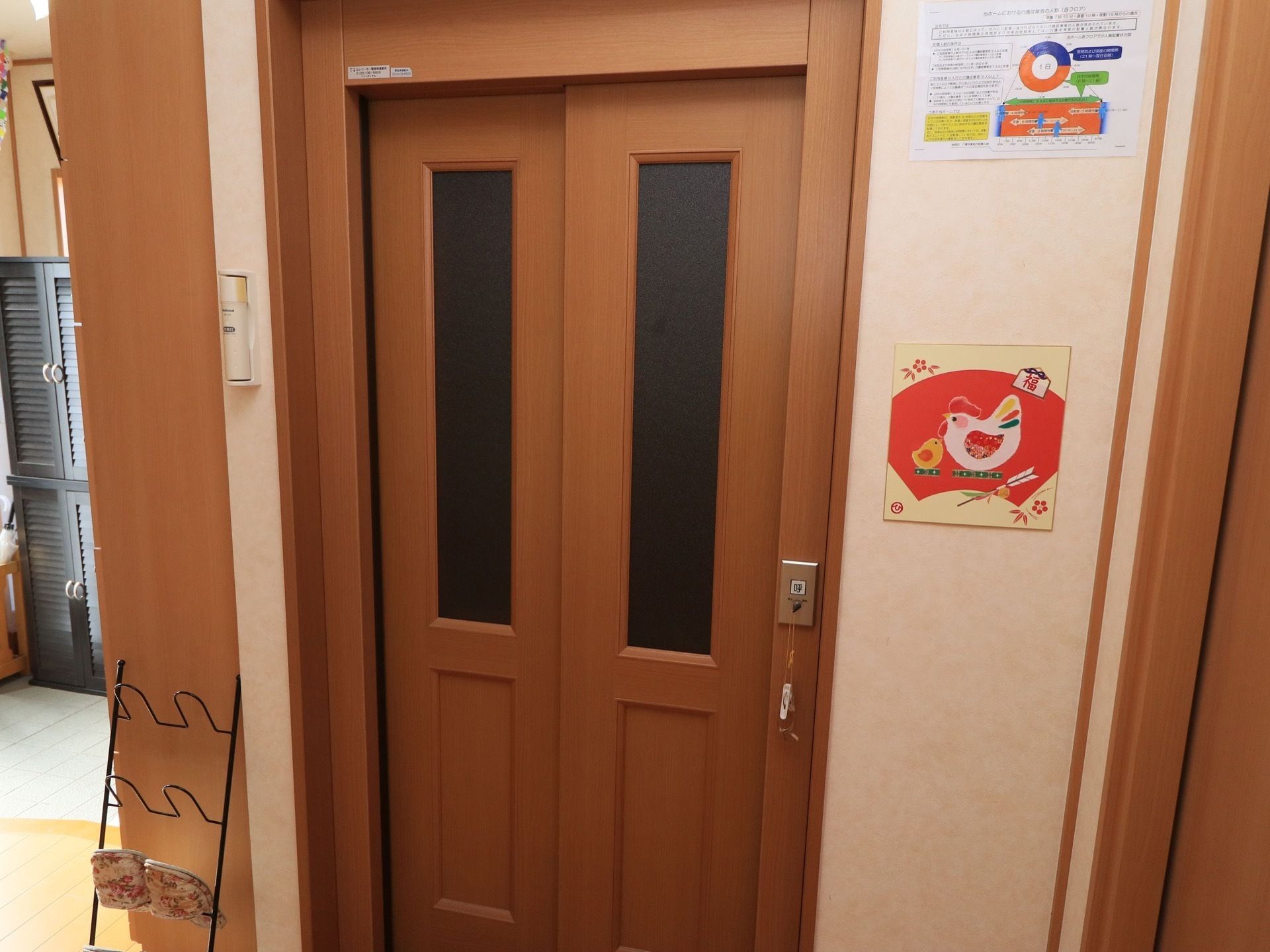 木製のドアとガラスののぞき窓がついているエレベーターがある。脇には来訪者様用のスリッパが置かれている。