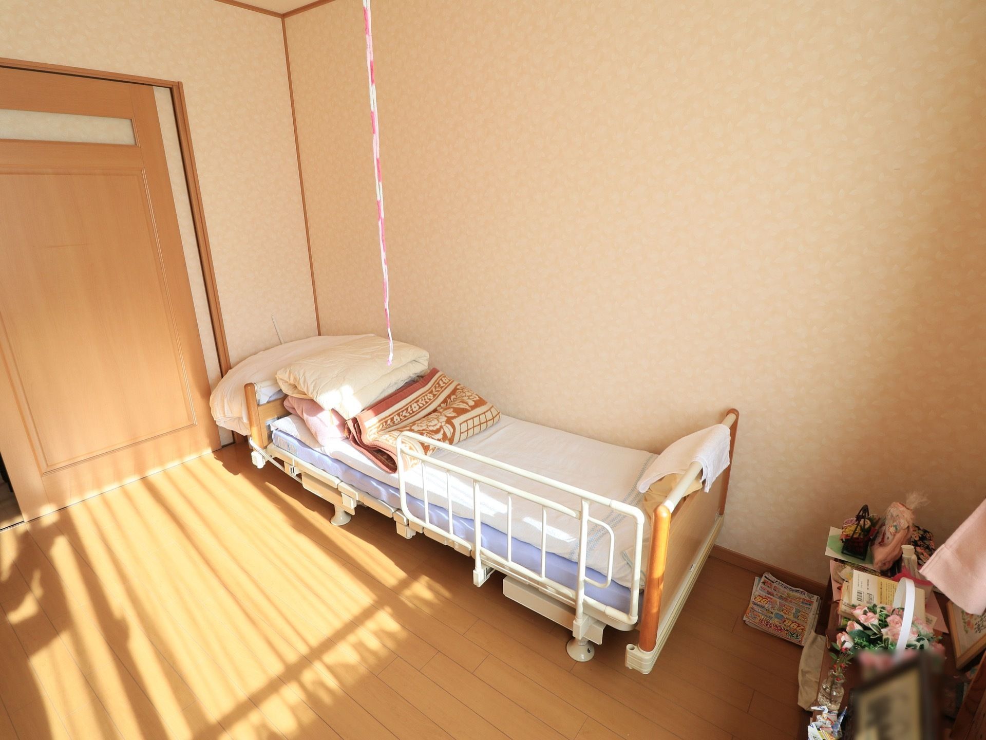 居室に明るい日差しが差し込んでいる、安全柵のついた介護用ベッドの上に布団が重なっておかれている。入り口の扉は引き戸式である。