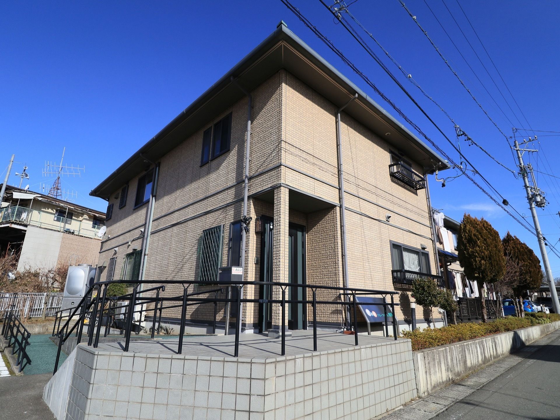 角地に立っている２階建ての施設の外観である。周りは一段高くなっており、柵と植え込みに囲まれている。玄関へとスロープが続いている。