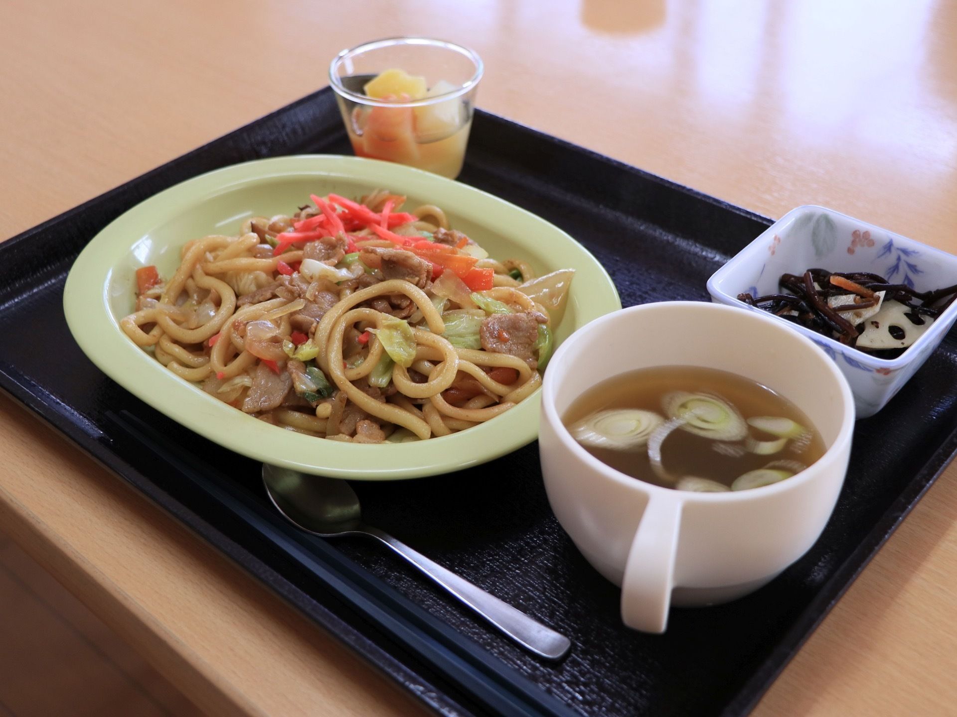 黒塗りのトレイの上に、焼うどん、スープ、山菜の煮物、デザートが置かれている。お箸とスプーンが添えられている。