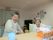 ２人の入居者様が並んで座っている写真である。右の座位をとるのが困難な入居者様には、肘置き付きの椅子と背当てクッションが提供されている。