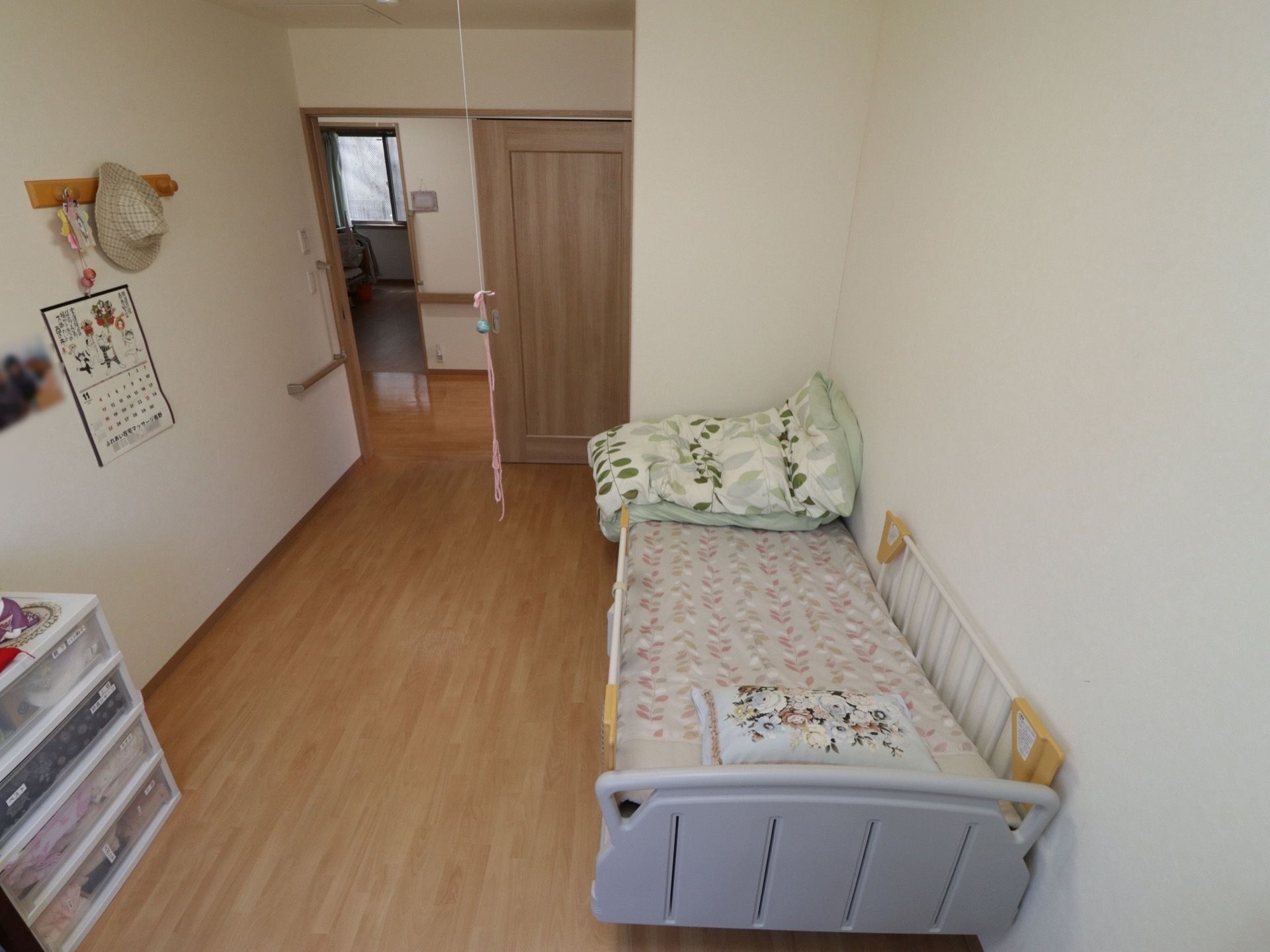 居室の入り口は木製のスライド式のドアになっている。壁側にベッドが１台設置されており、両側にベッド柵が設けられている。