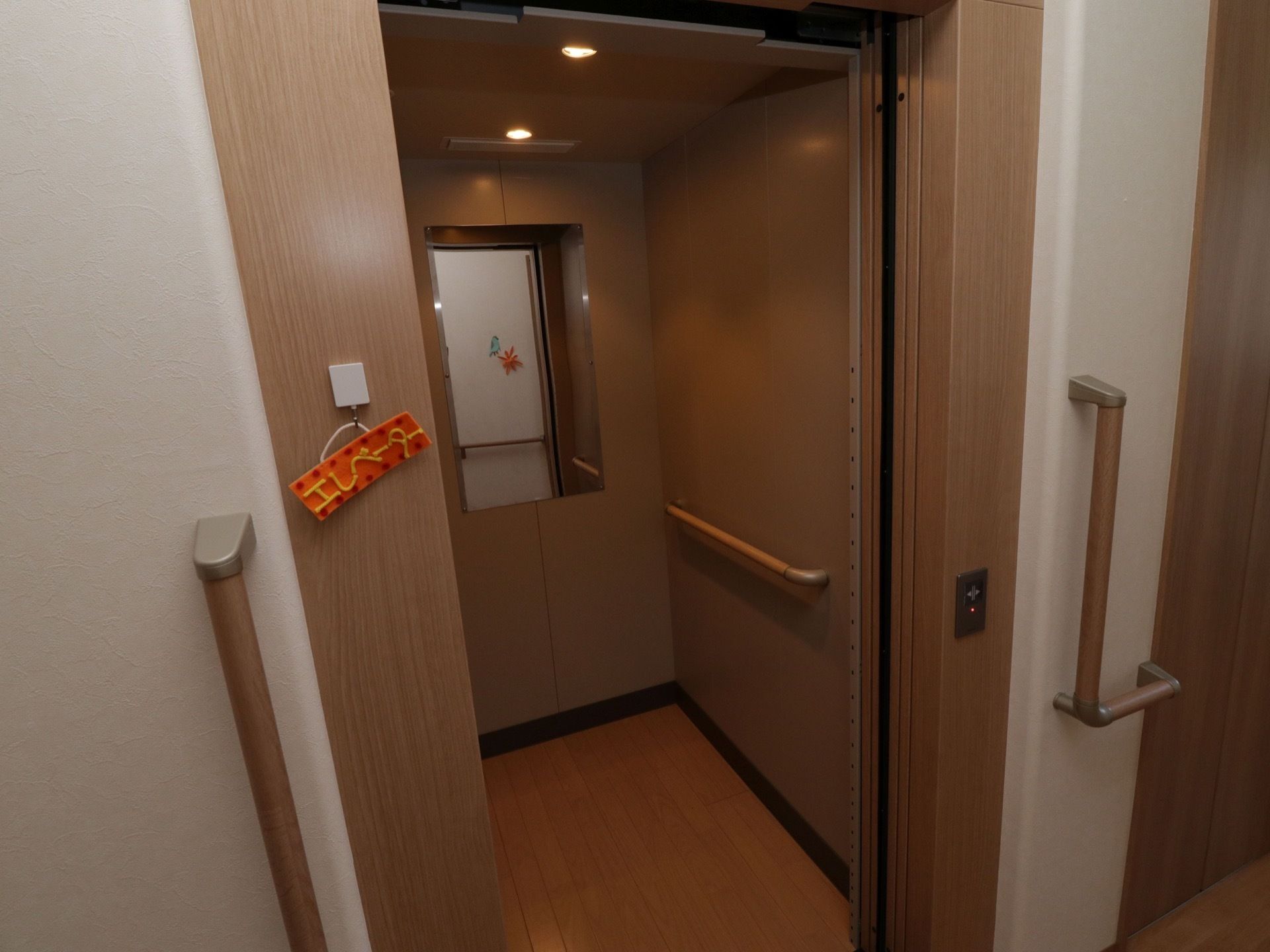奥行きのあるエレベーターで、庫内は落ち着いた色合いである。奥側に鏡が設置され、右側の壁に手すりが設けられている。
