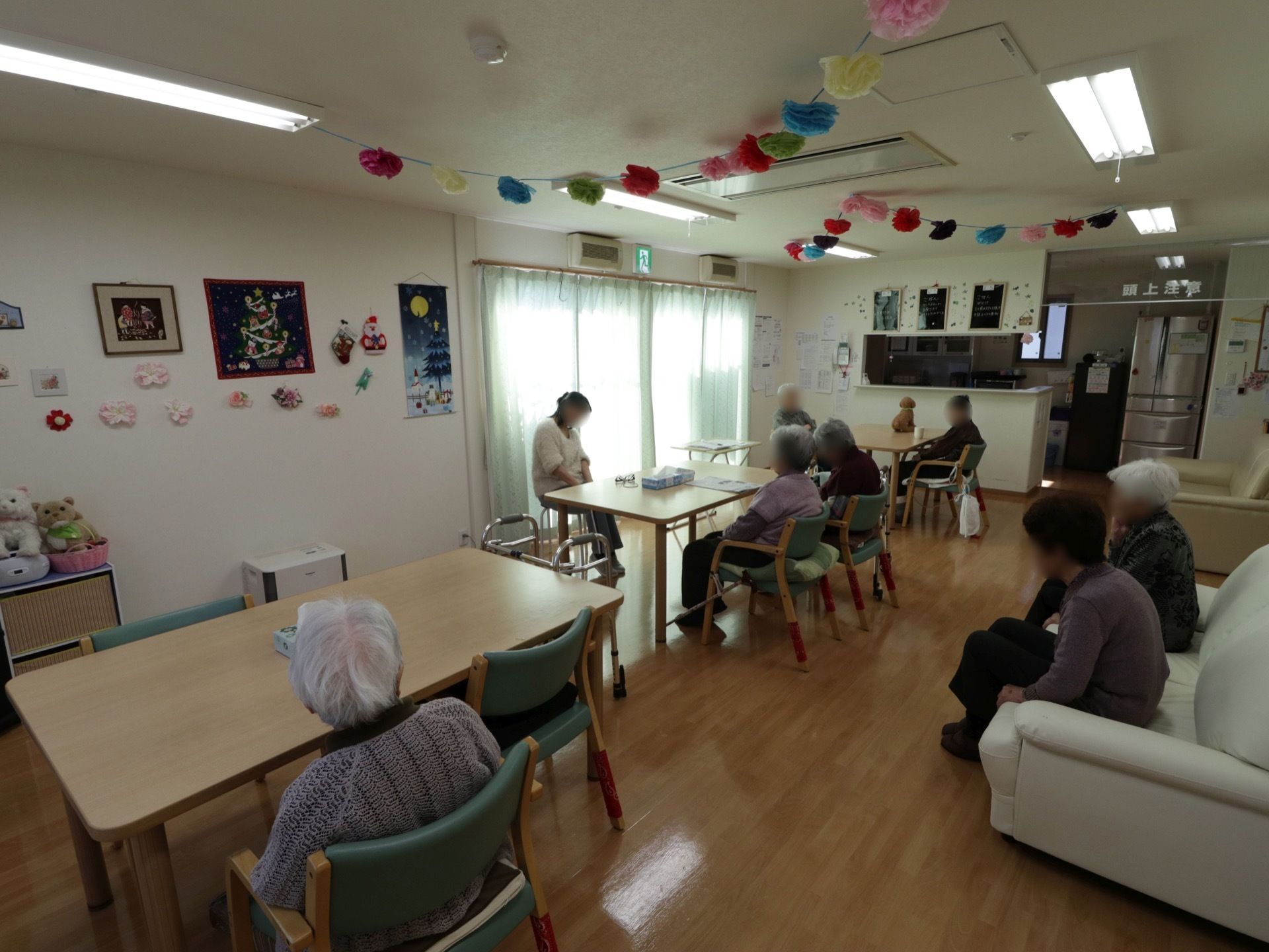 窓側の椅子にスタッフが座り、向かい合う形で入居者様が椅子やソファに座って、首の体操などを行っている。