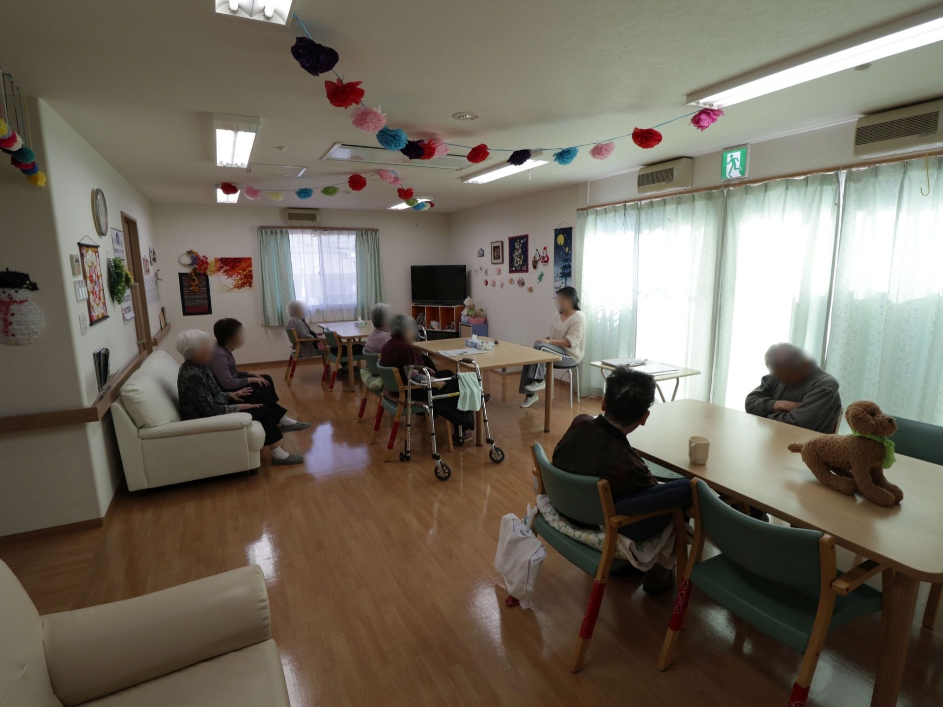 ４人掛けのテーブルと椅子が並べられているスペース。壁際にはソファがある。大きな窓があり、天井や壁には飾りつけがされている。