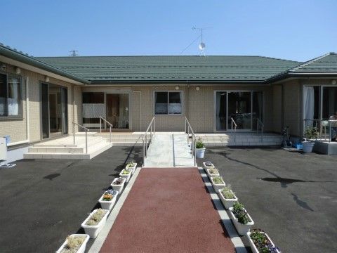 平屋建ての本施設の入口には、手すりが取り付けられた階段と、緩やかなスロープがある。各所に花を植えたプランターを配置している。