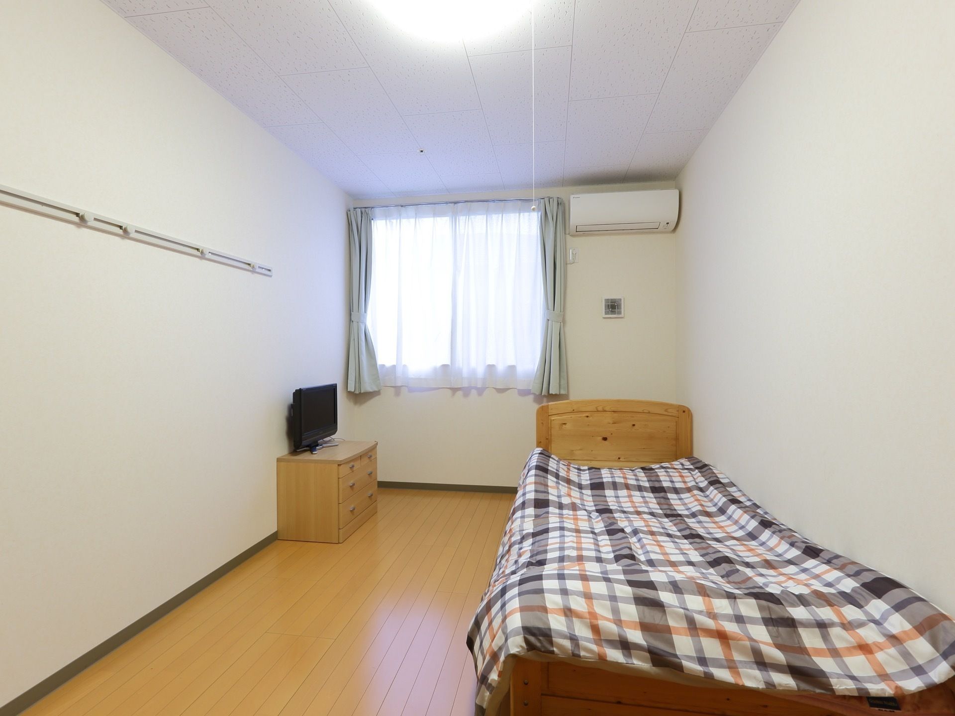 広々とした居室となっている。家具は優しい色で統一されている。エアコンを設置している。床はフローリングである。