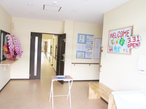 バリアフリー設計の平らな床のエントランス。間口が大きい黒いドアの先には廊下が続いており、壁には手すりが付いている。